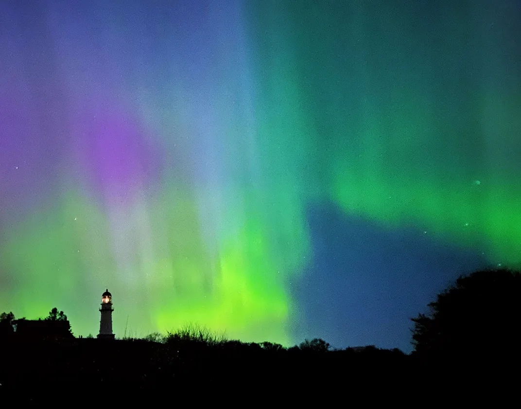 green, purple and blue northern lights above a lighthouse