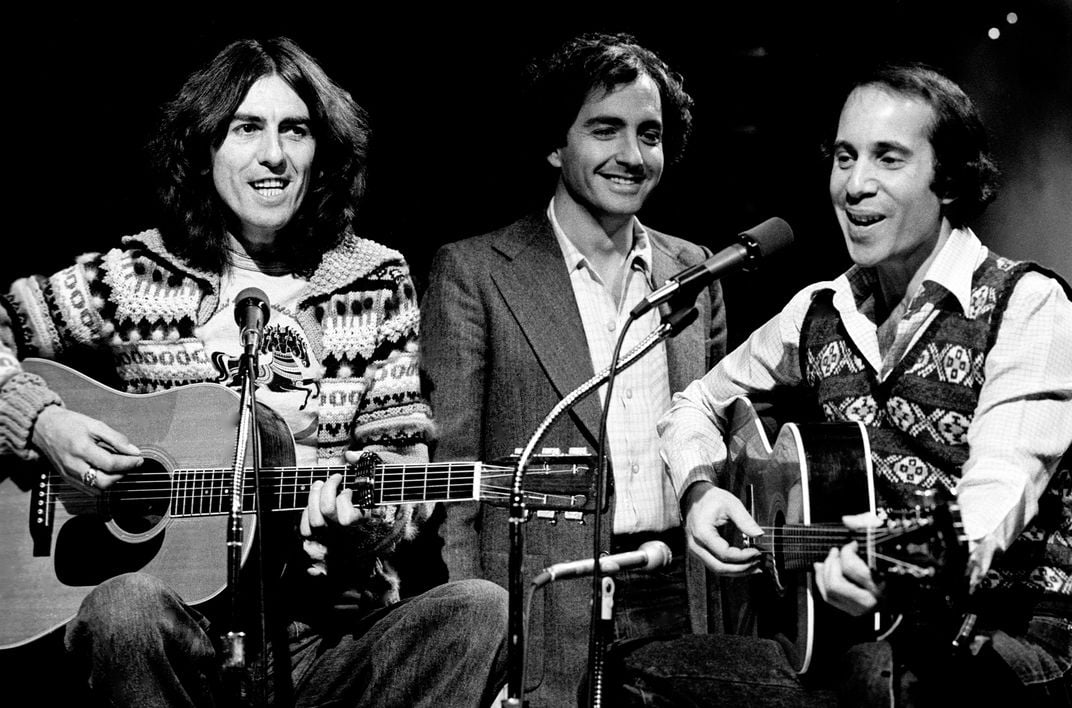 George Harrison (left) and Paul Simon (right) record songs for "Saturday Night Live" on November 19, 1976, with Lorne Michaels (center) looking on