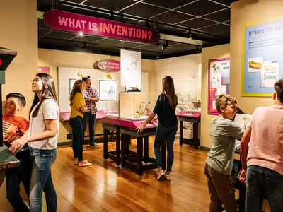 Seven people- adults and children- interact with the Nation of Inventors exhibition gallery